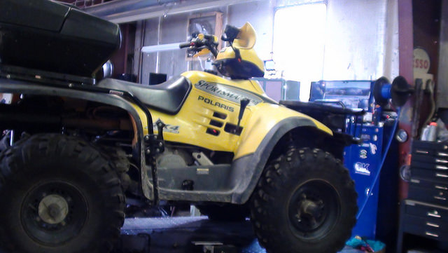 A photo of a yellow ATV in a garage. 