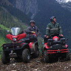 Five Quads and their riders are lined up against beautiful blue mountains.