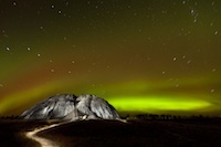 An amazing view of the the northern lights, stripes of yellow and green, over a small mountain.
