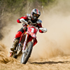 a guy riding around a turn on a dirt bike with dust billowing