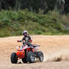 an ATVer riding through sand with forest in the background