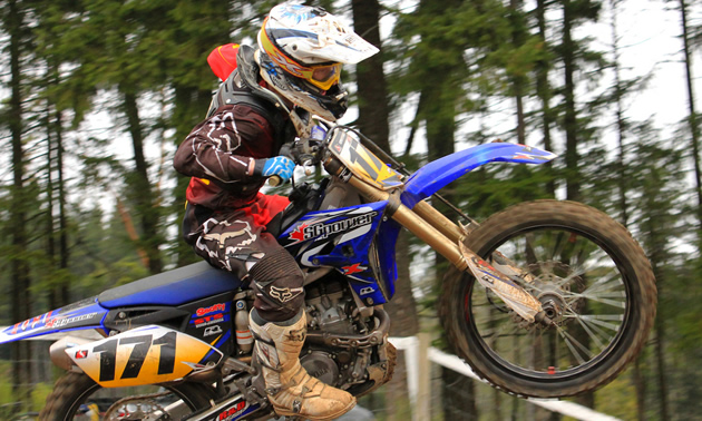 Photo of a guy riding a blue dirt bike. 