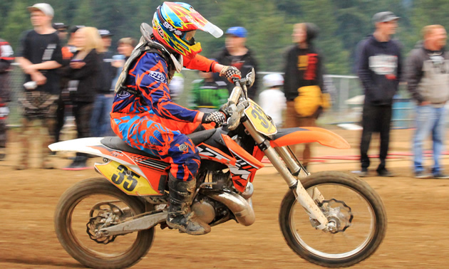 Photo of a guy riding an orange dirt bike with spectators watching him. 