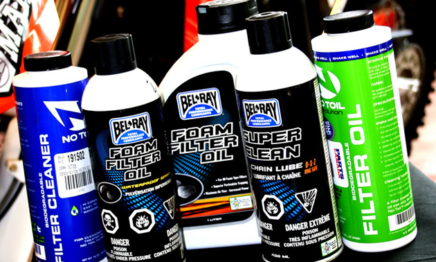Products for oiling and cleaning air filters lined up with a bike in the background. 