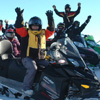 26 women sitting on their parked snowmobiles with their hands in the air 