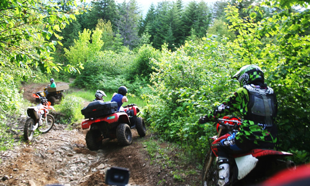 Depending on their skill sets, participants at the Summer Solstice Ride could choose to ride technical terrain or go on a more casual ride. — Brook Evans photo Dirt bikers watch as a person on a red ATV drives through ruts on a dirt trail.