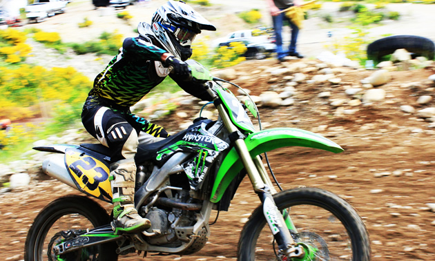 Photo of a guy riding a green dirt bike. 