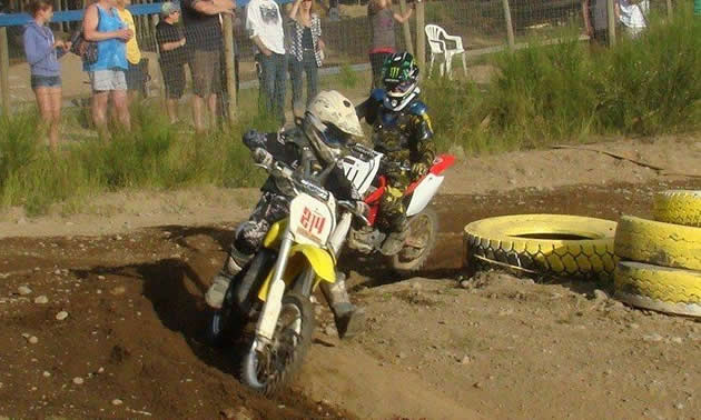 Photo of two young kids on dirt bikes coming around a corner.