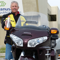 A grey haired man holding a message in a bottle and standing by a purple Honda Goldwing. 