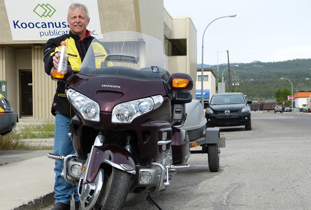 A grey haired man holding a message in a bottle and standing by a purple Honda Goldwing. 
