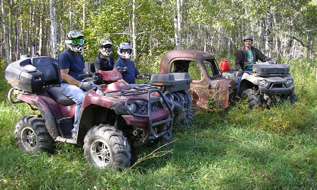 Several people pose on their muddy ATV's for a picture.