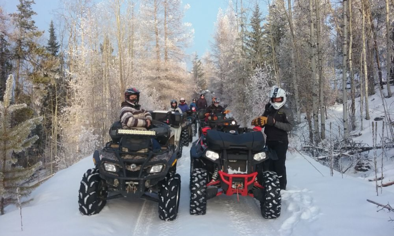 A row of ATVs ride next to each other on a snowy trail. 