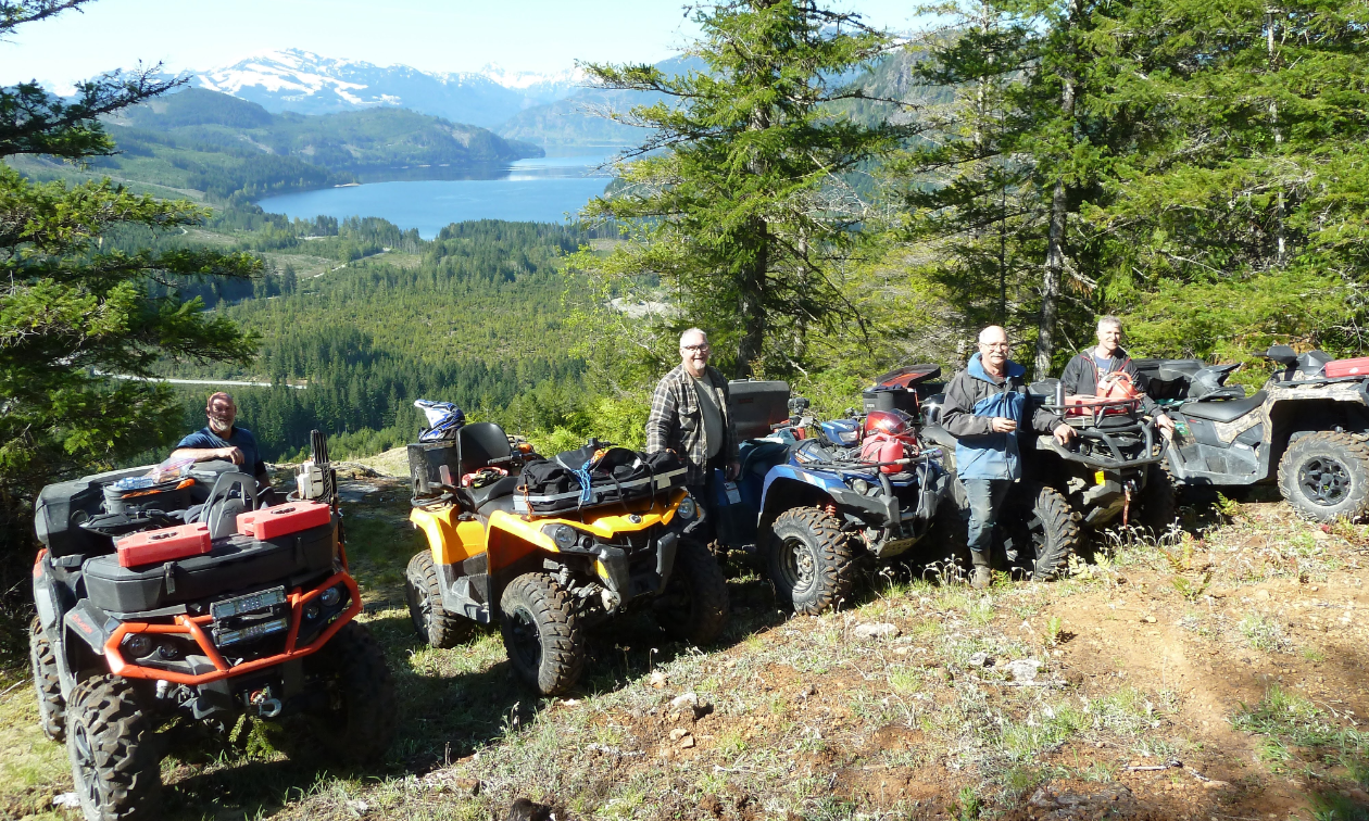 A lineup of ATVers standing next to their ATVs on the side of a mountain. 