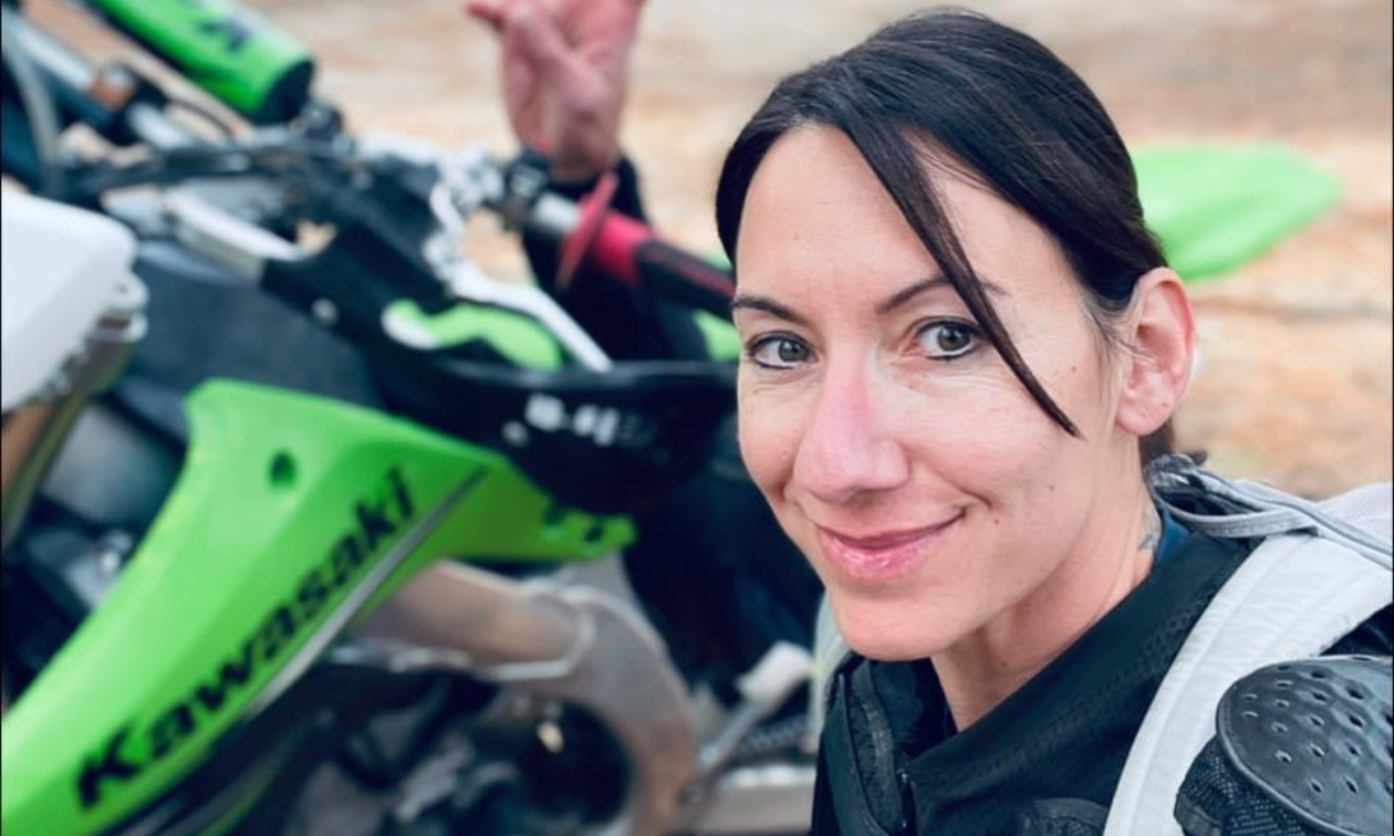 Alysha “Axxe” Vlahovich smiles next to her green Kawasaki dirt bike. 