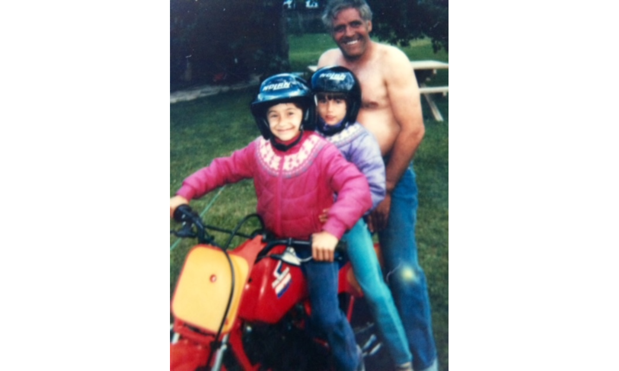 Two girls ride on a small red dirt bike with a man sitting on the back too. 