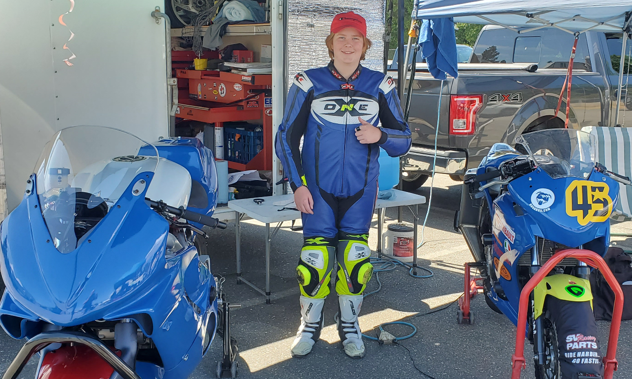 Andrew Van Winkle smiles while standing next to his blue Honda CBR250R under a tent in a parking lot. 