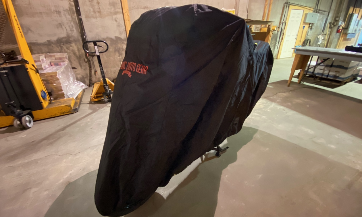 A black Badass Moto Ultimate All Wx Waterproof Motorcycle Cover covers a motorcycle in a garage.