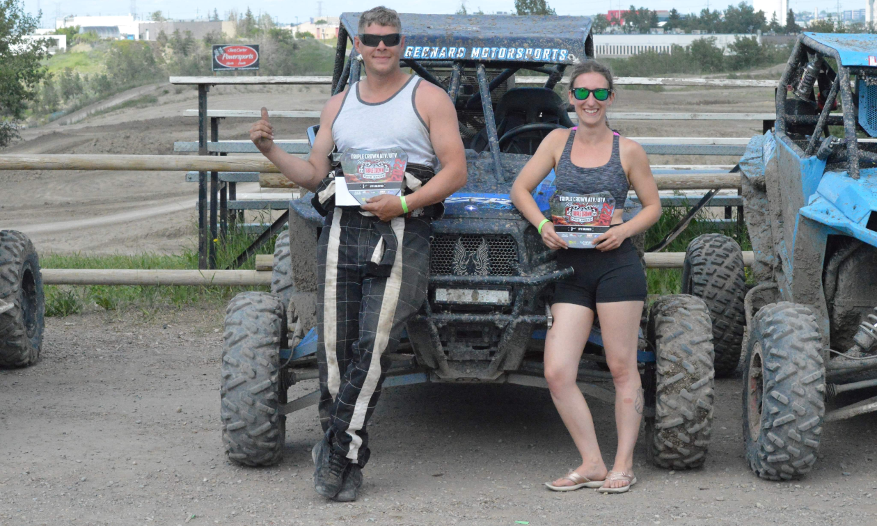 Richard Bernard and Denise Misner stand in front of a Polaris RZR ATV and smile with trophies won at the Triple Crown Race Series.