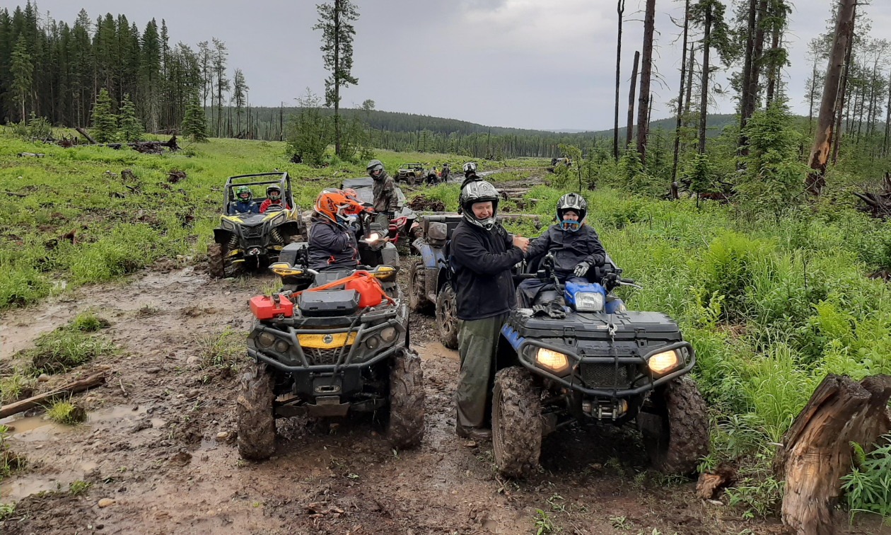 Several ATVs are parked on a muddy road in a wooded area. 