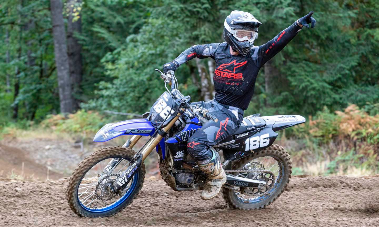 A dirt bike rider holds up his hand in celebration as he rides across a track.