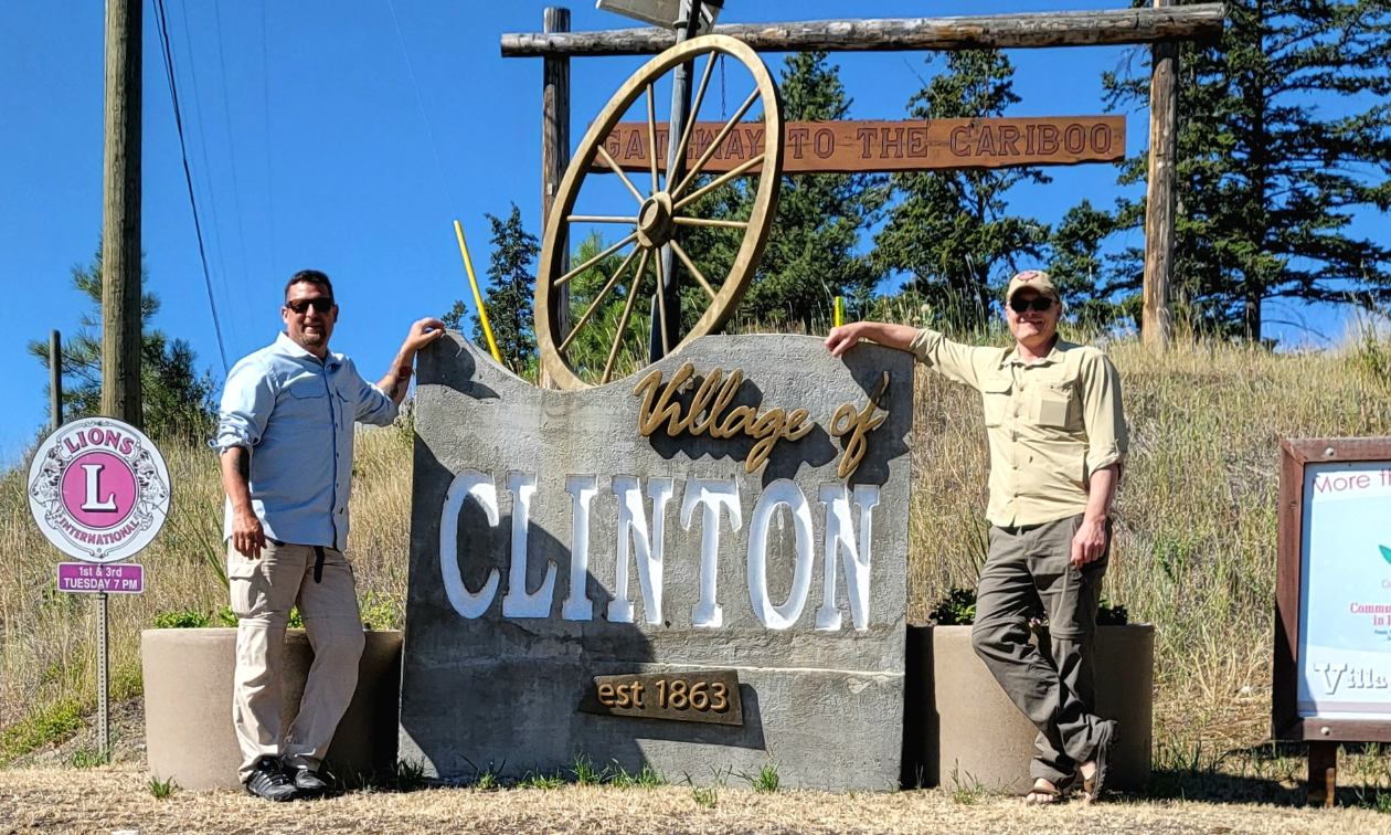 John Giannisis and his friend, Antony Francis, pose in from a sign that says Village of Clinton.