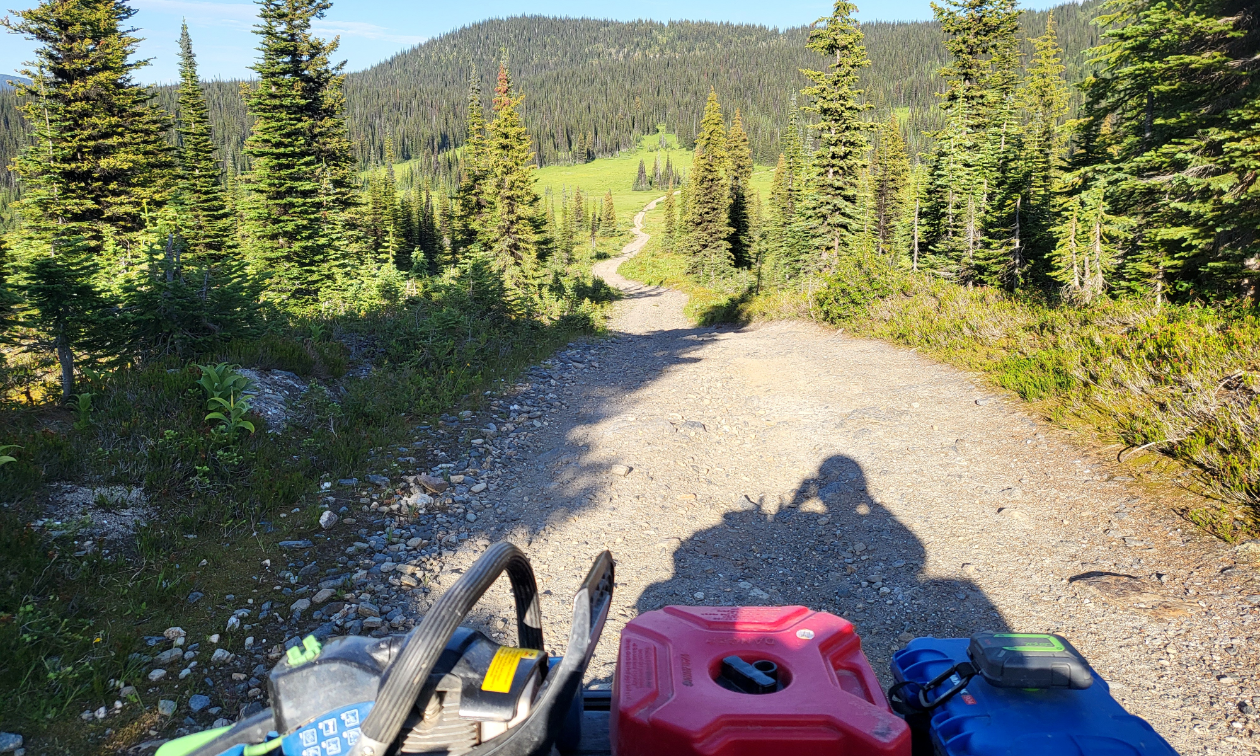 An ATV trail descends into a lush, green valley below a mountain. 
