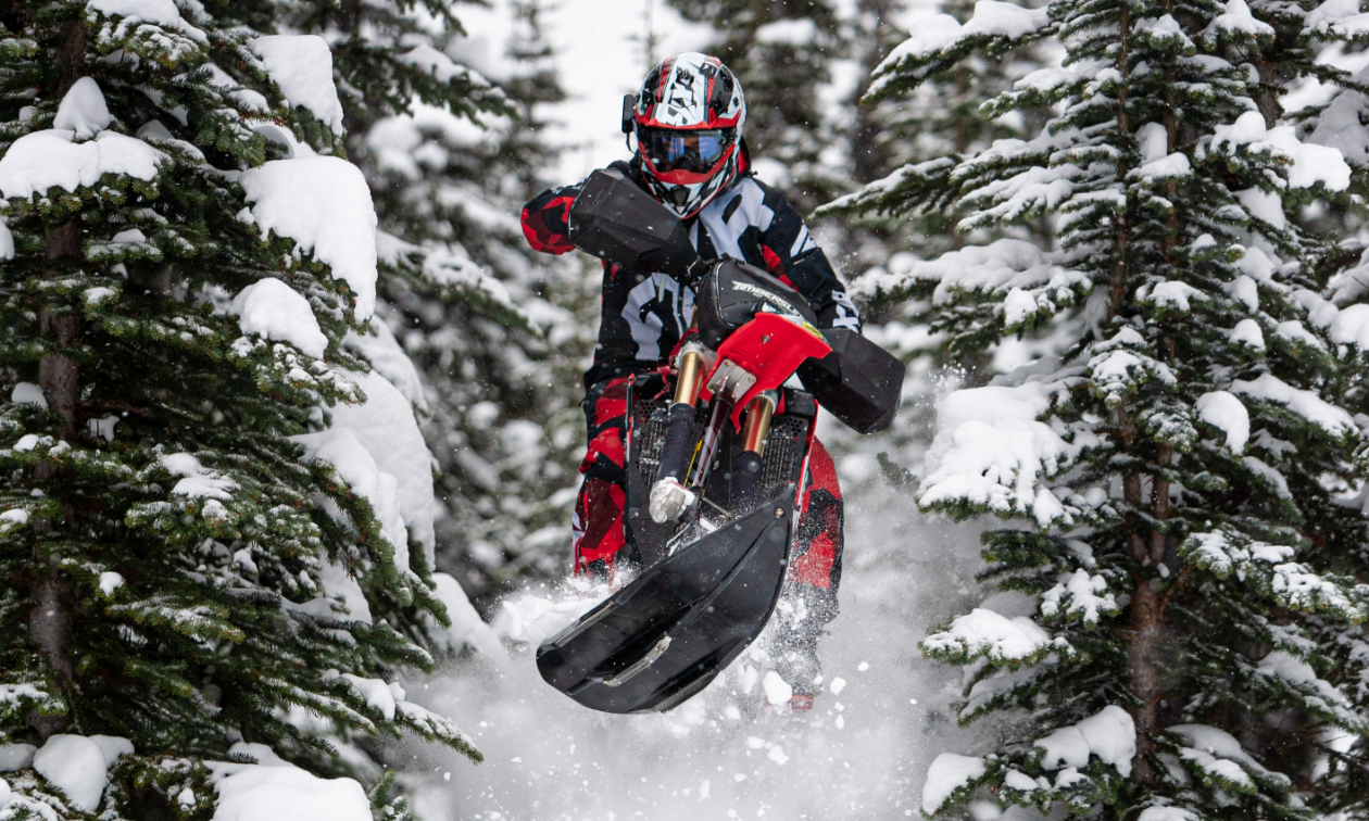 Curtis Hofsink does a big jump between snowy trees on his red 2018 Honda CRF450RX.