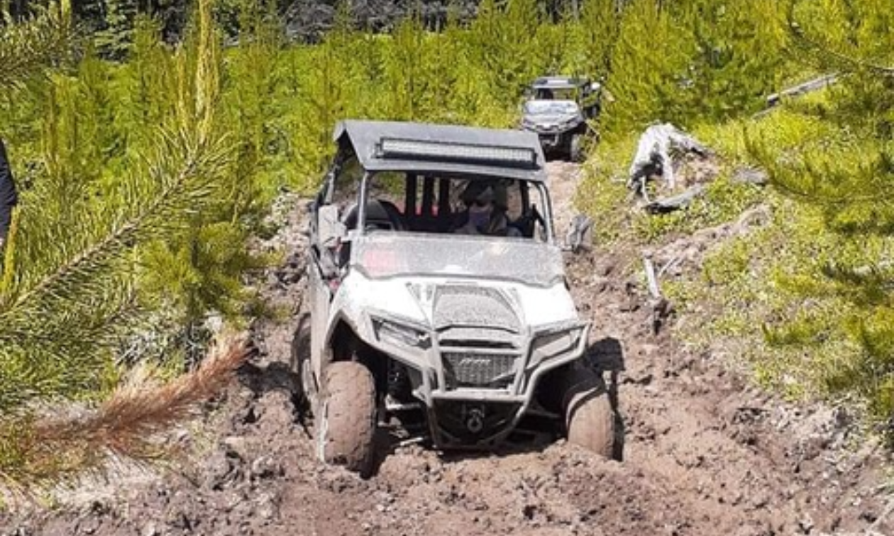 A side-by-side ATV plows through a muddy dirt road. 