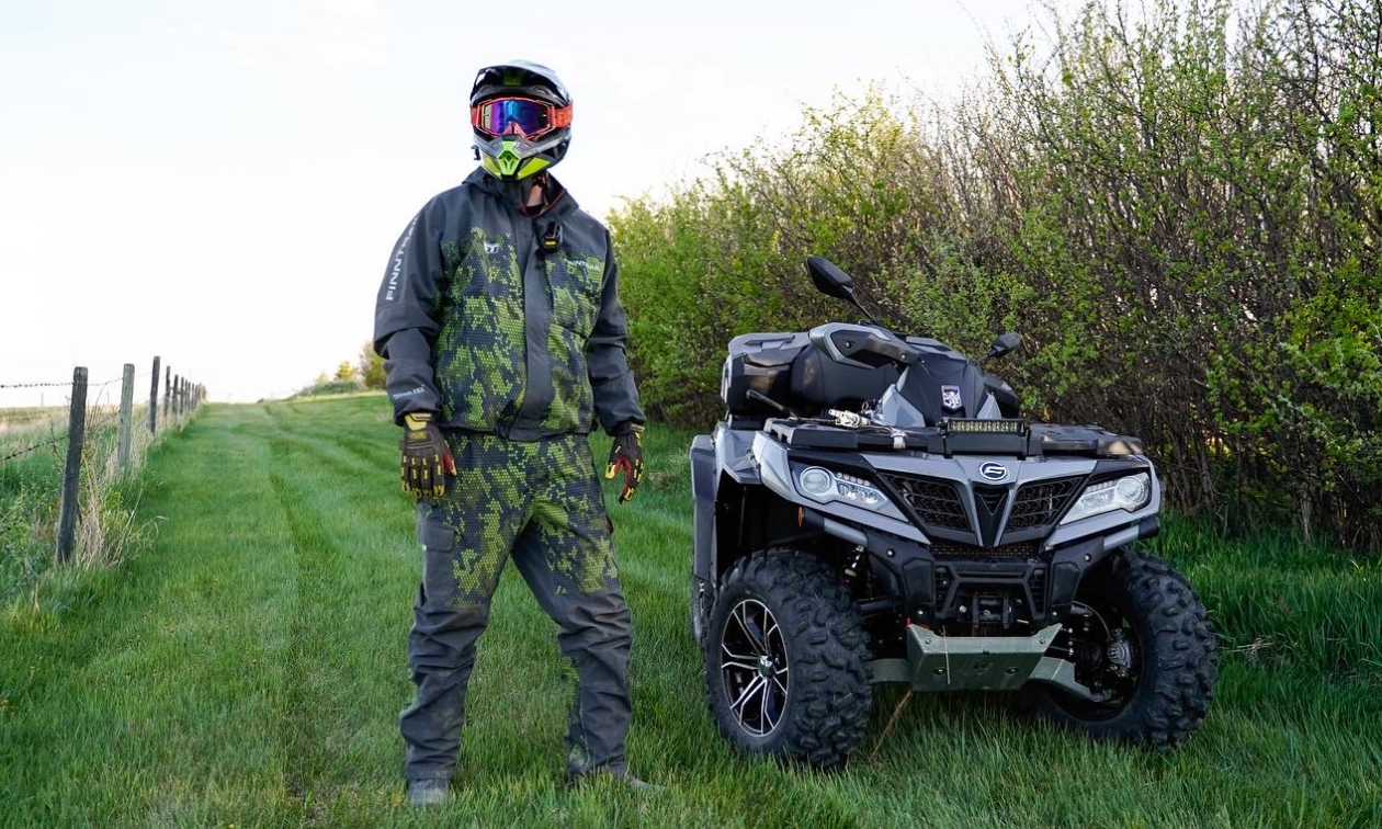 Dan Kruse stands beside his ATV next to a row of trees on one side and a fence line on the other. 