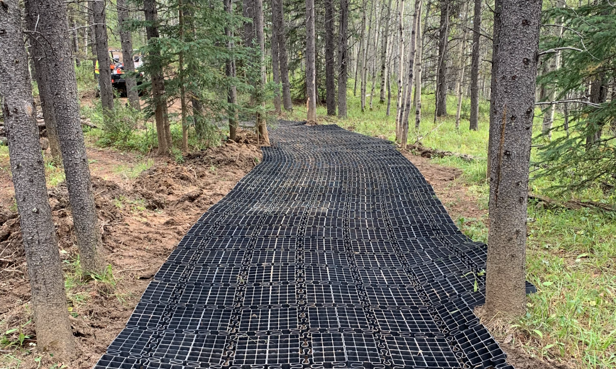 Black rig mats are linked together along an ATV trail and winds through trees. 