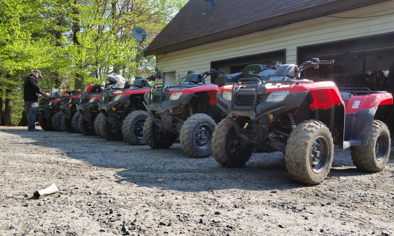 Five red ATVs are in a row in front of a garage. 