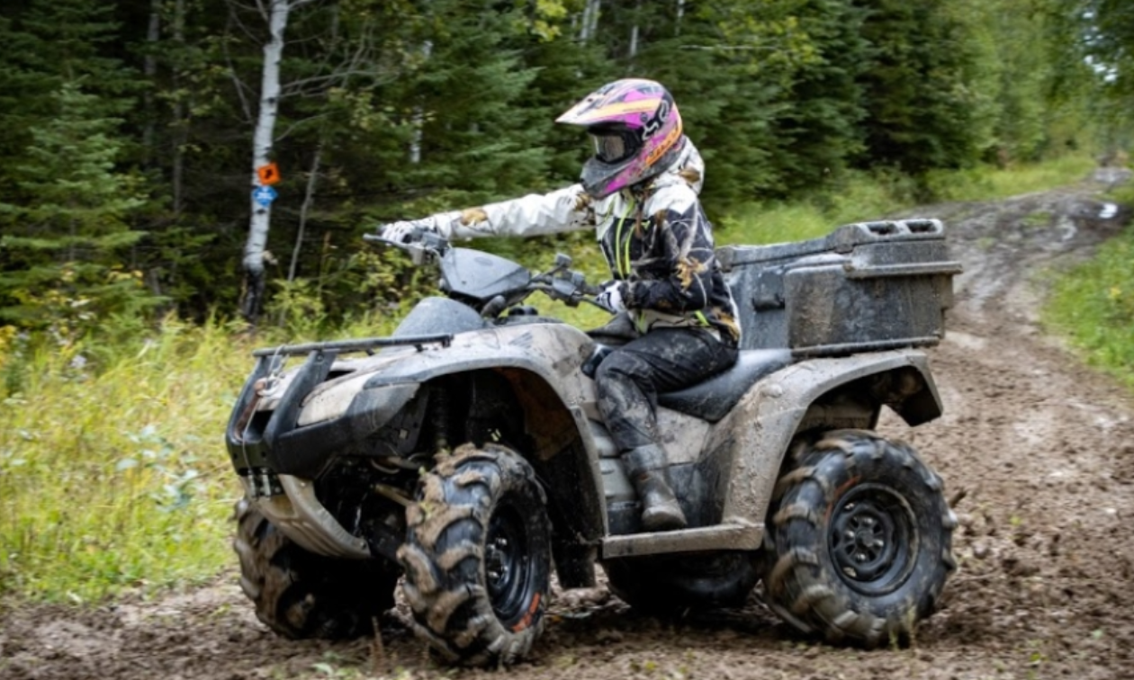 A woman rides an ATV through a muddy trail in the forest. 