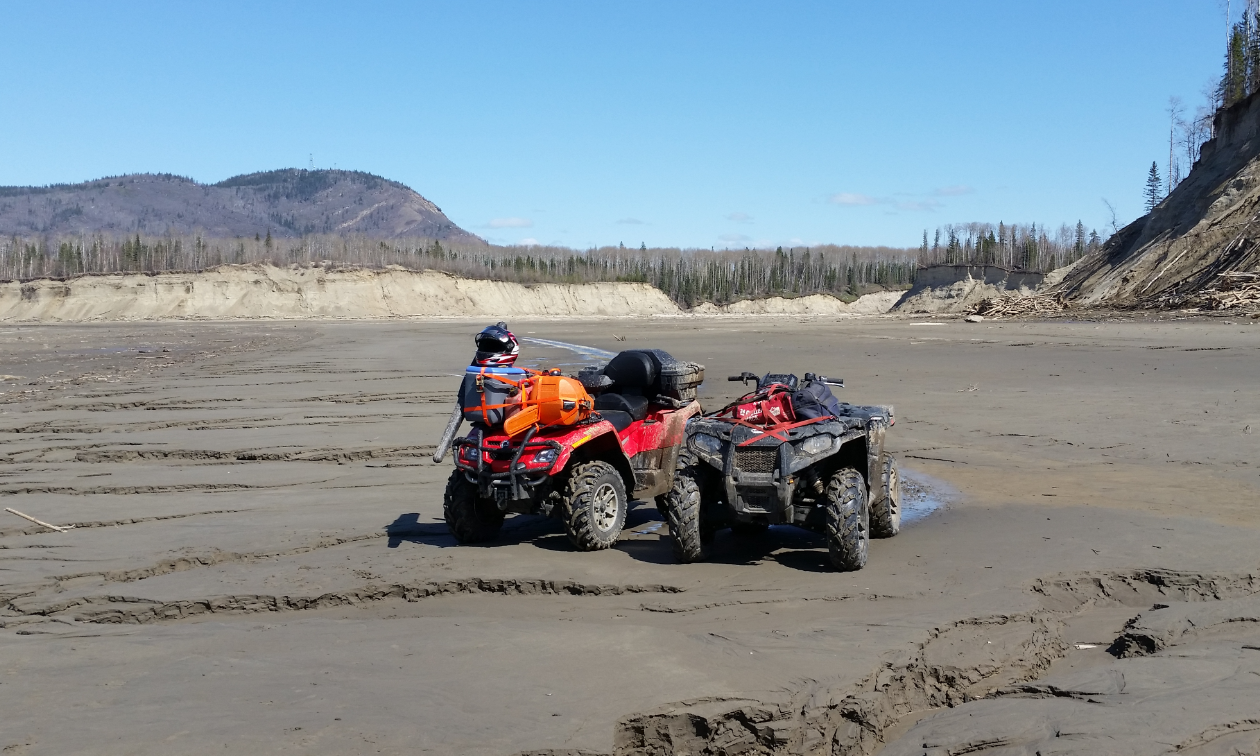 Two red ATVs are parked on a sandy beach area. 