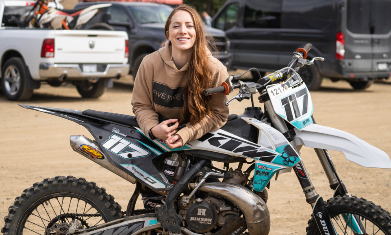 Kela Louise leans over her black and turquoise 2017 KTM 250SX dirt bike. 