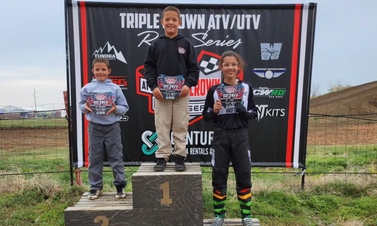 (L to R) Theo (age 8), Isaac (age 10) and Savannah (age 12) Kumson. They wear black clothes with their logo on their chests, and red, green and yellow lines wrapped around their ankles.