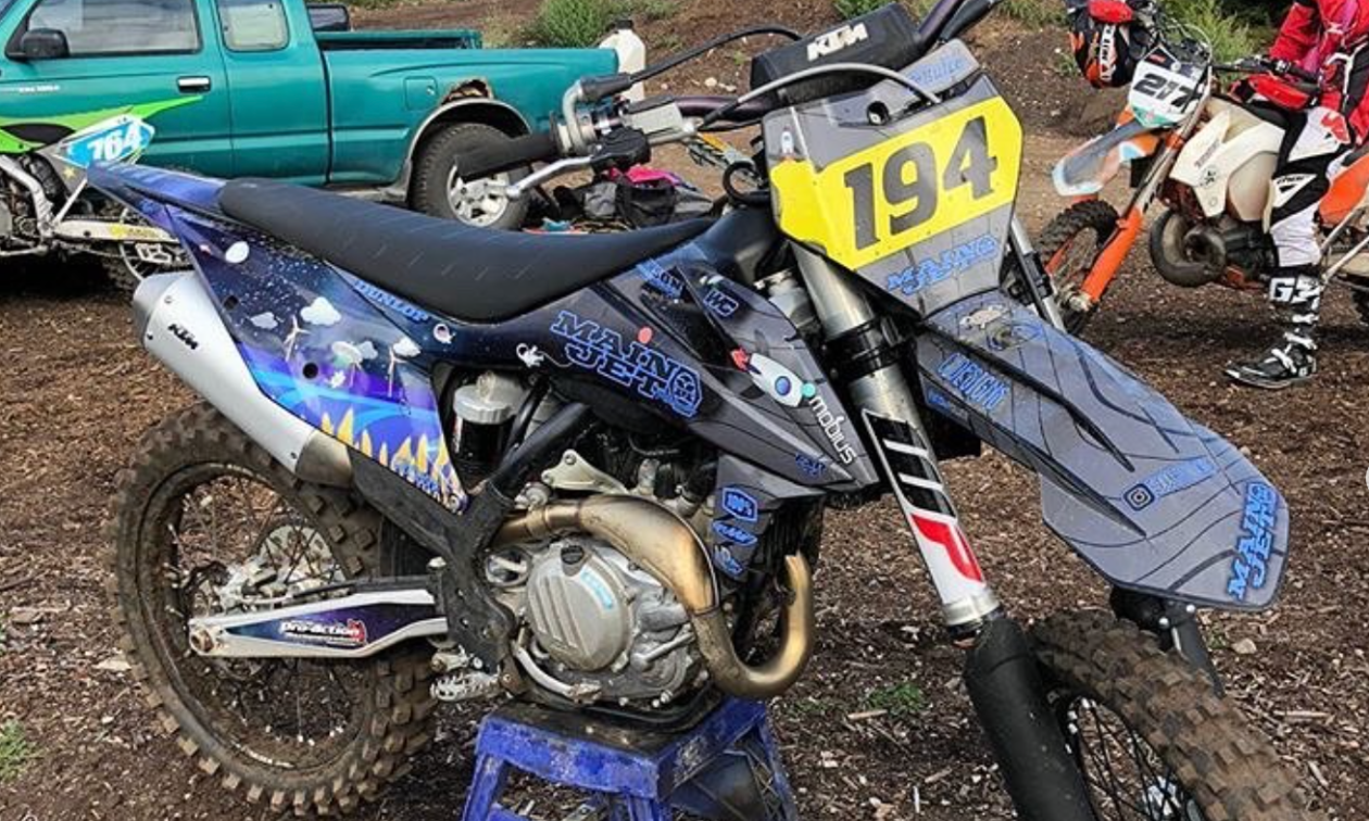 A blue and black dirt bike has a sled wrap of an alien invasion. 