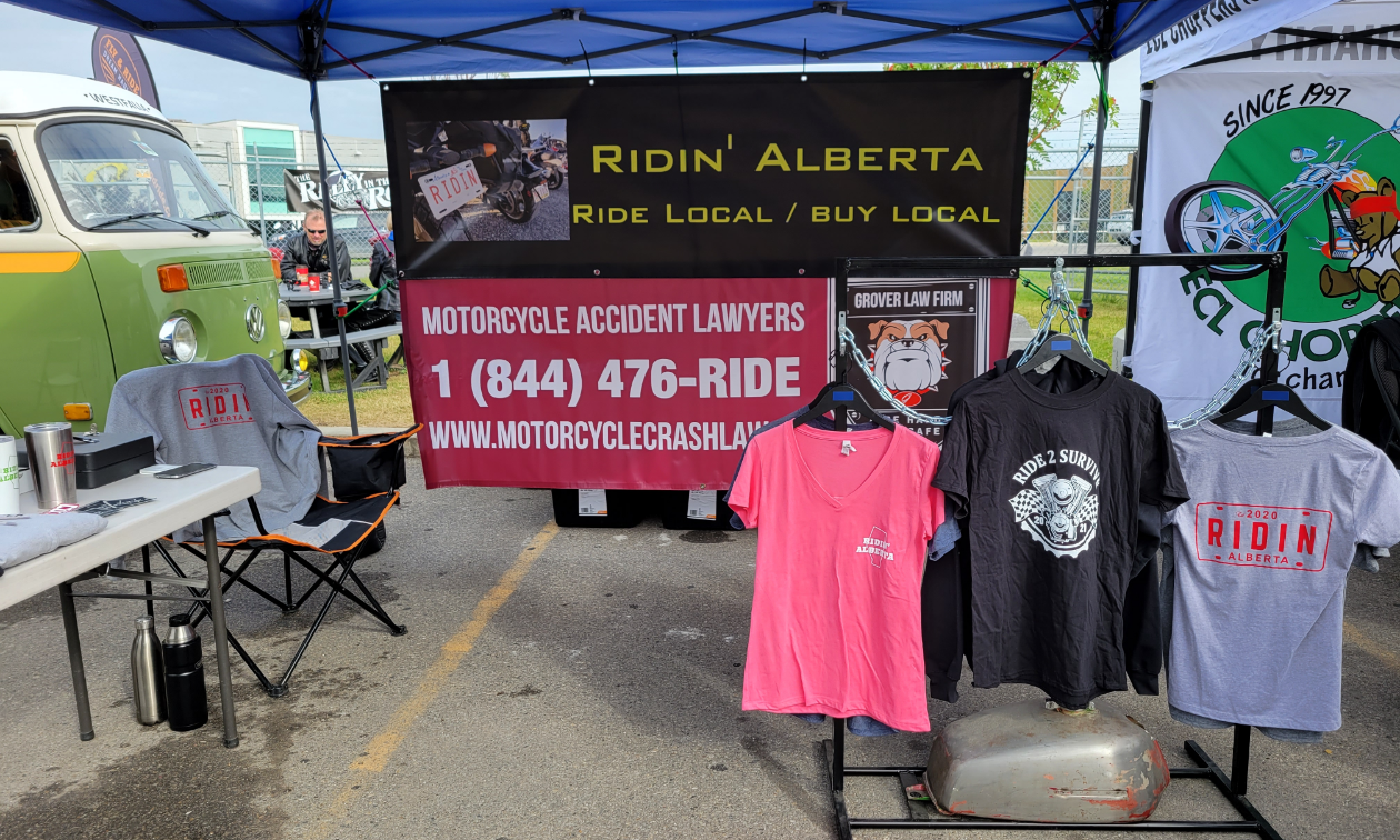 A tent booth is set up in a parking lot with T-shirts available for purchase for Ridin’ Alberta. 