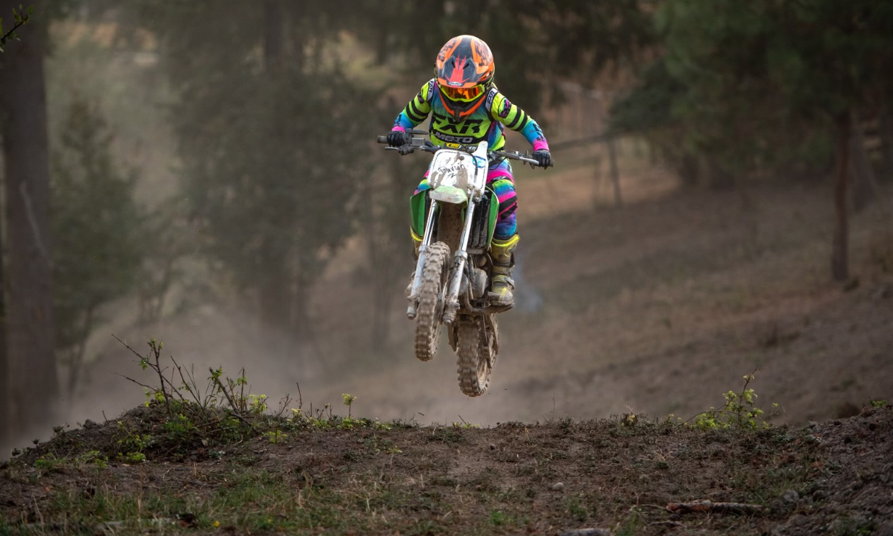 Davian Clayton gets air over a jump on a dirt bike track. Davian wears neon green and blue gear. 
