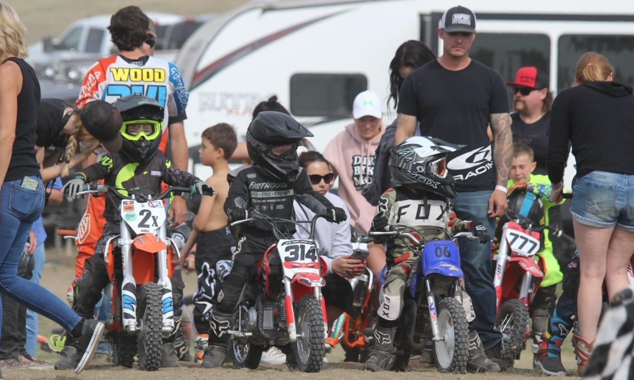 A row of children on motorbikes getting ready to start a race on a dirt track. 