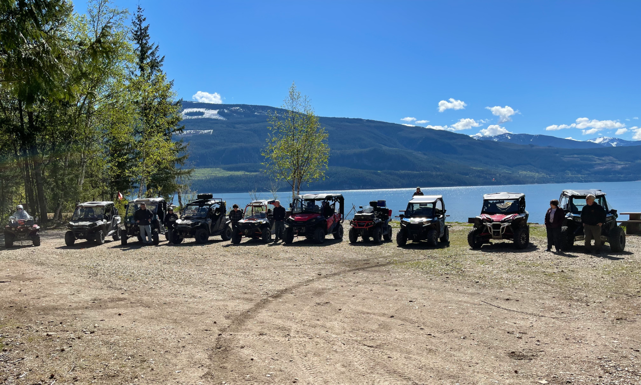 A row of ATVs lined up next to a lake in front of a mountain.