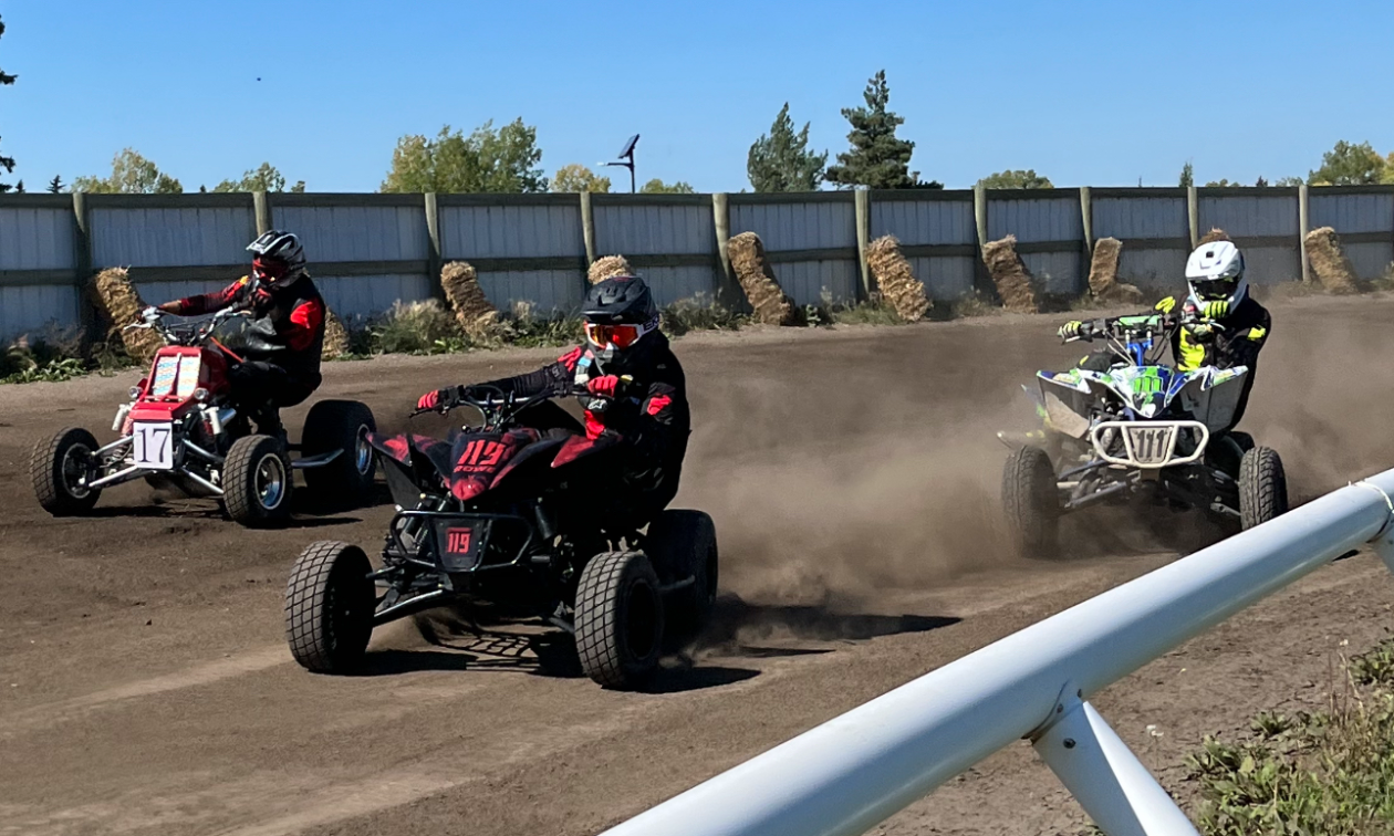 Three quads race around a corner on a dirt track in Alberta. 