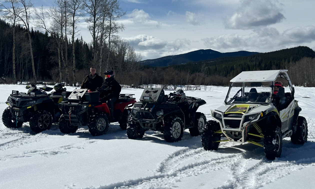 A row of four ATVs are parked in a snowy field in Alberta on a partially cloudy day. 