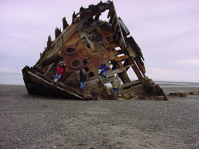 Phil Megyesi and his friends standing in front of the hull of an old ship washed up onto the shore. 