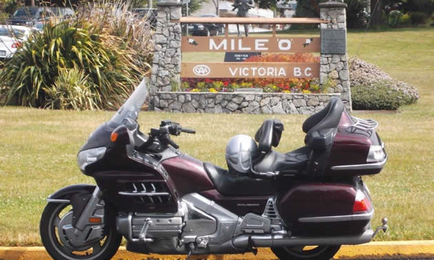 A motorcycle parked in front of Mile 0 sign in Victoria. 