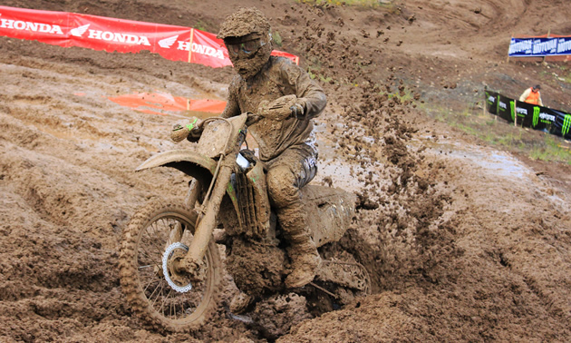A guy on a dirt bike covered in mud. 