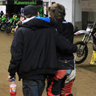 A father helping his son across the dirt track. 