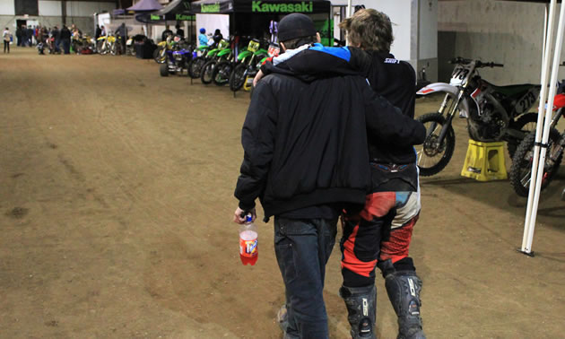 A father helping his son across the dirt track. 
