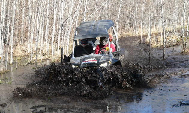 A side by side going through deep mud. 
