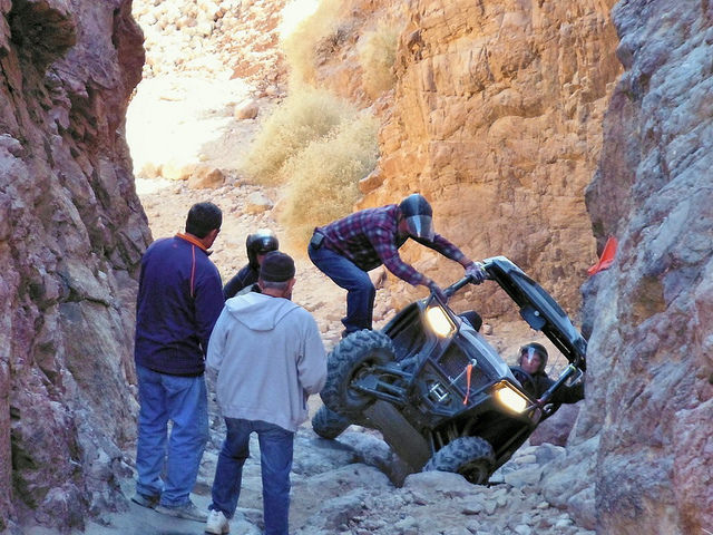 An ATV got stuck on a rough trail and there are three people trying to help get it out.