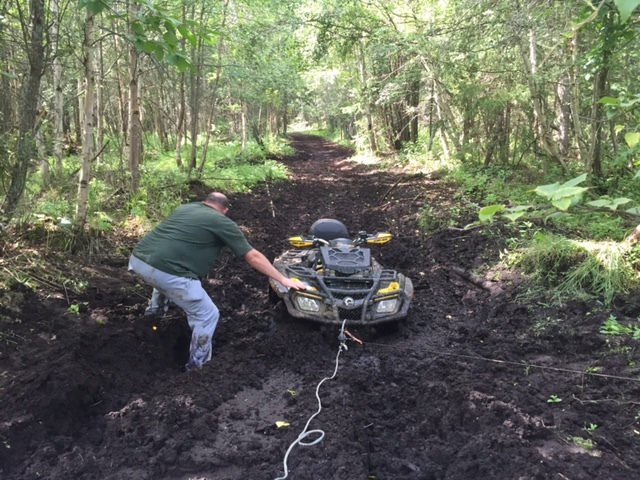 Pulling an ATV by winch out of a mud hole in the centre of a trail.